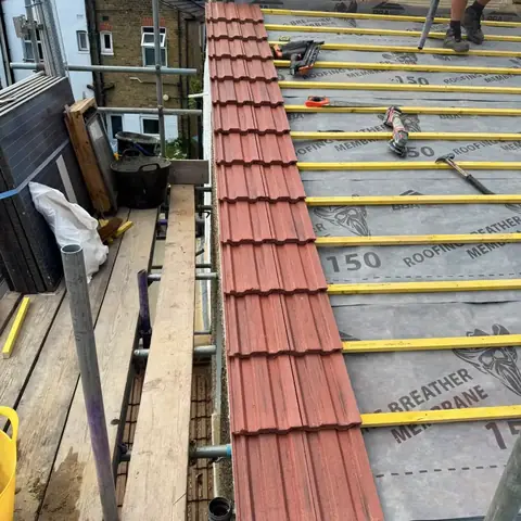 Red tiles going on along the verge of the roof over new breathable membrane