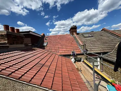 Newly tiled red roofs on a terrace of houses in Bromley, under a blue sky