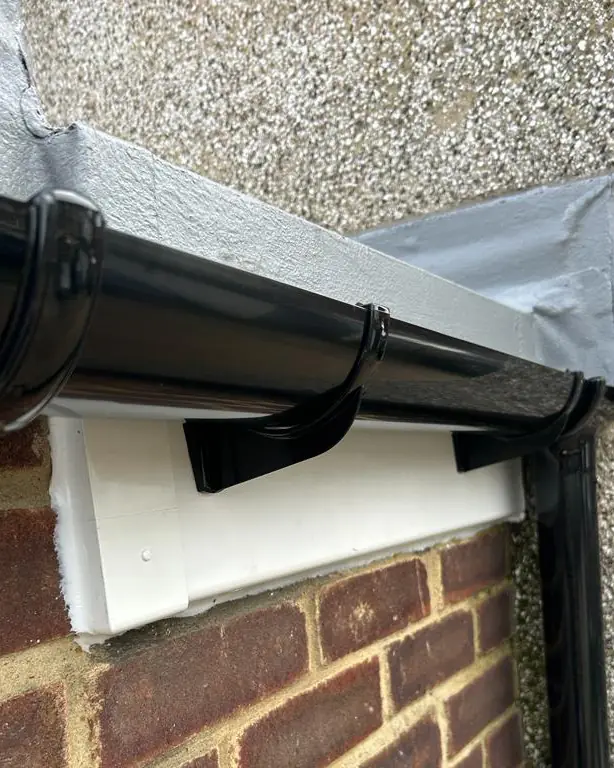 The same roof edge repaired, with a white fascia and new black gutter